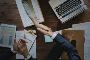 Two people shaking hands over a stack of papers.